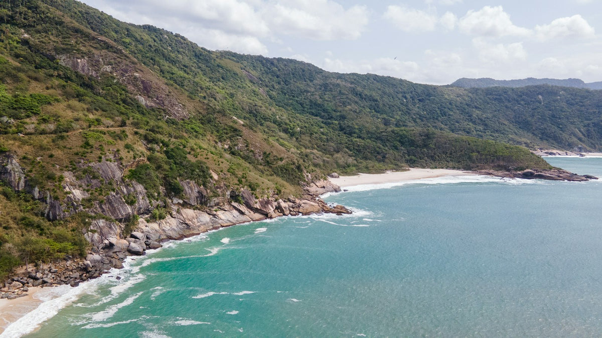 A quiet beach backed by green, forested hills on the coast of Rio de Janeiro