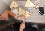 Guest adding beads to the straps of a pale yellow bikini with a pink flower print