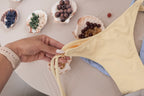 Hand tying a beaded charm onto a pale yellow bikini, with shells of wooden beads on the table